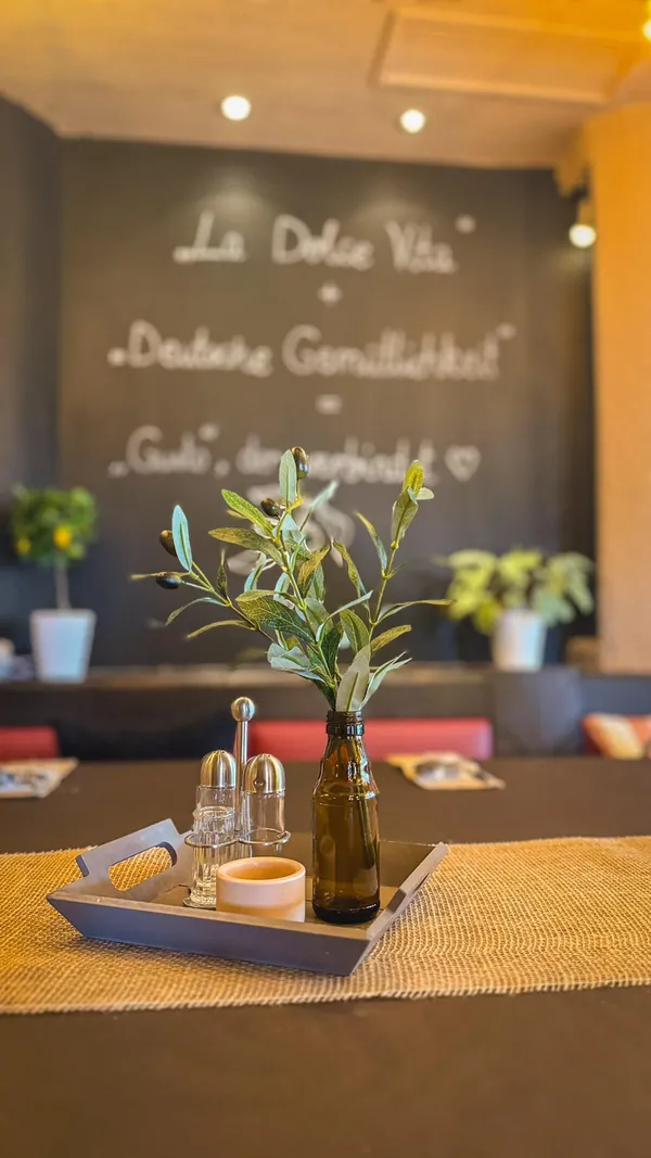 Olivenzweig in einer Flasche auf dem Tisch, im Hintergrund die Kreidetafel mit La Dolce Vita
